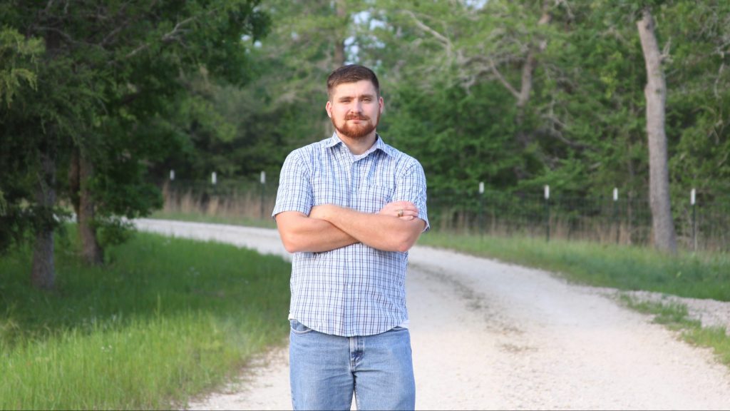 Josh Tutt standing cross armed in a collared shirt on a dirt road.